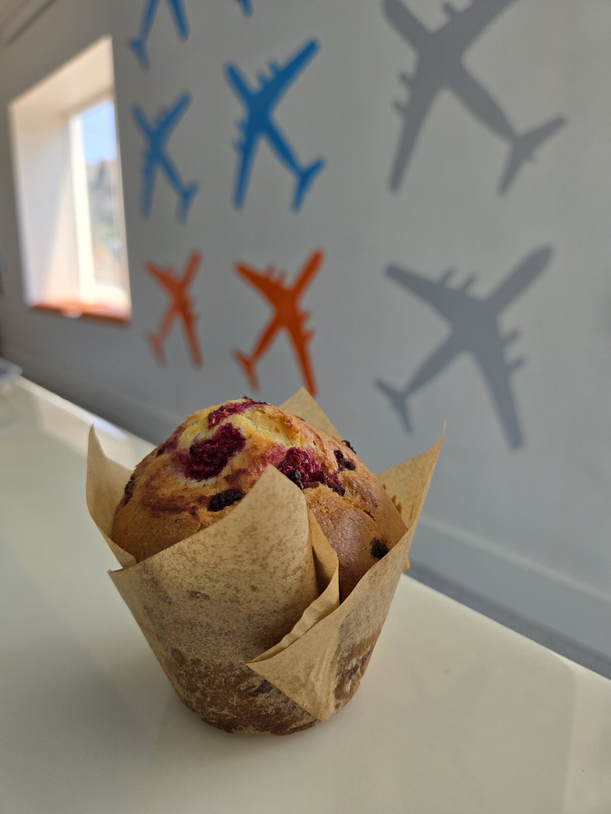 A berry muffin in a paper wrapper inside the café.
