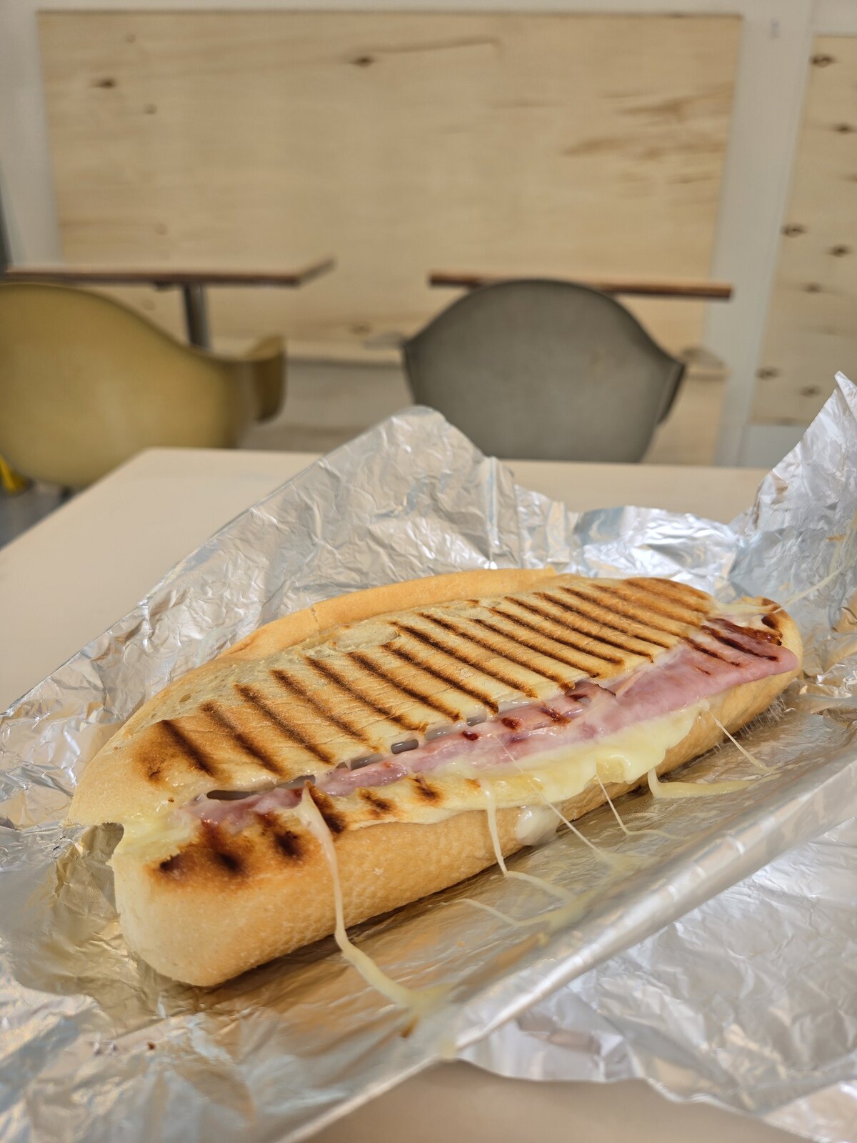 A long toasted sandwich with melted cheese in an open foil wrapper.