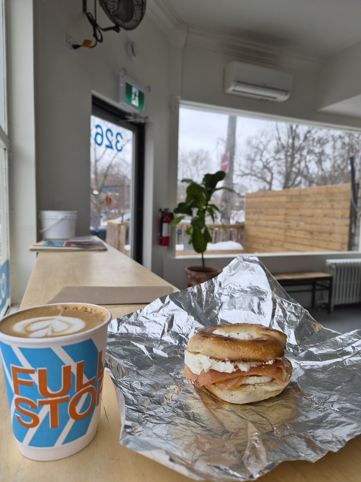 A bagel sandwich and a Full Stop coffee beside the café window.
