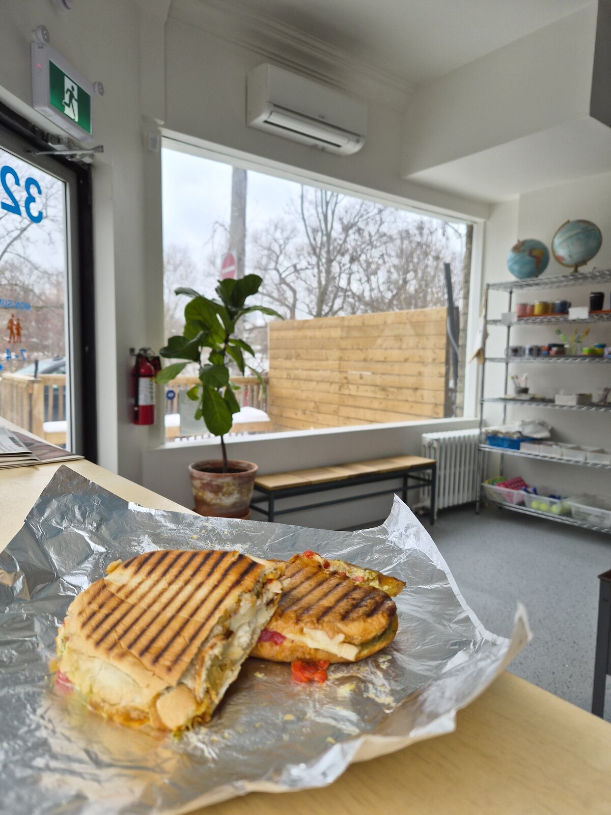 Two grilled sandwich halves in foil beside the café window.
