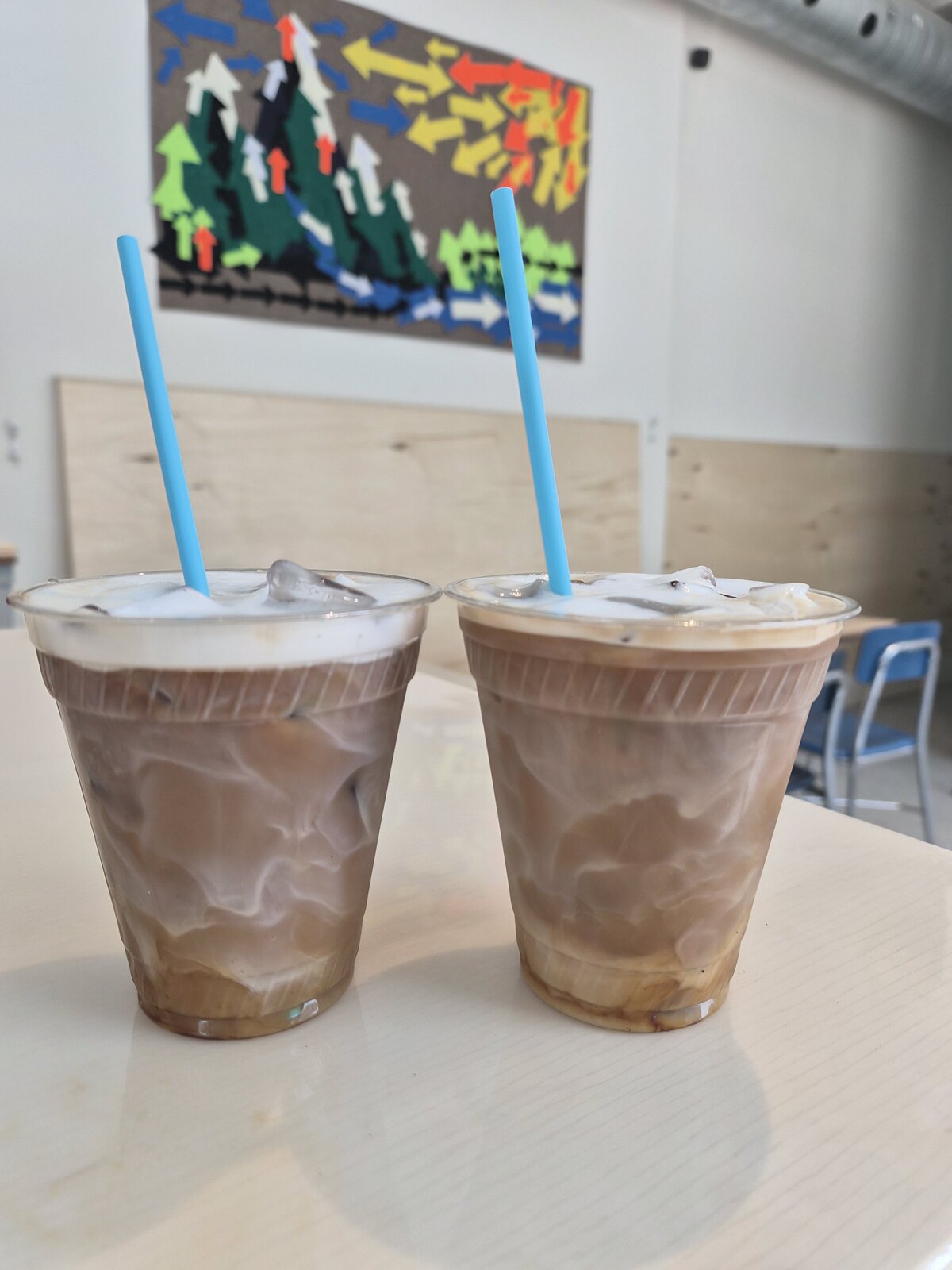 Two iced coffees in clear cups with blue straws on a café table.