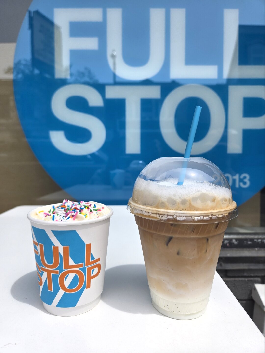 Two Full Stop drinks in front of the café window sign.