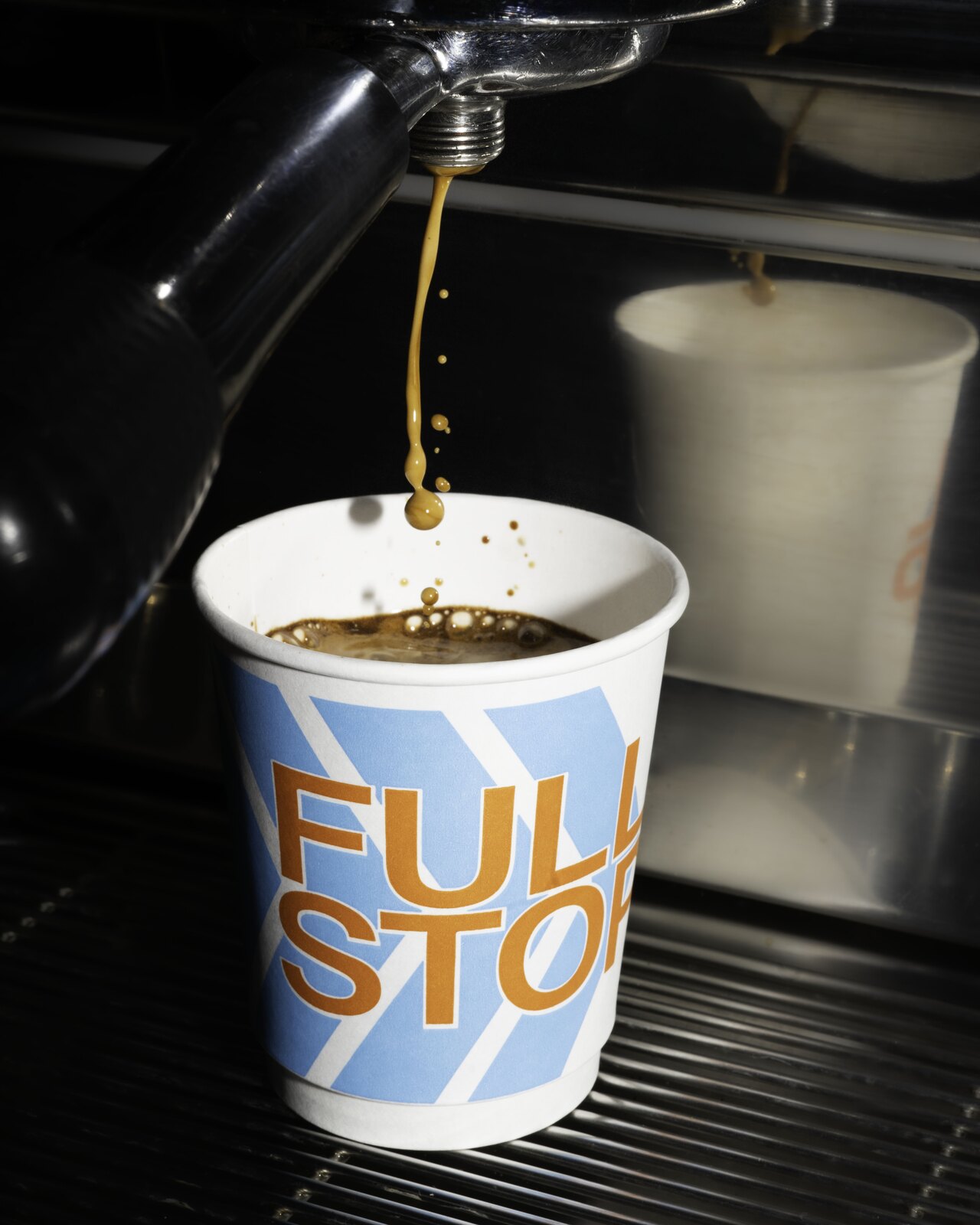 Espresso pouring from a coffee machine into a Full Stop paper cup.