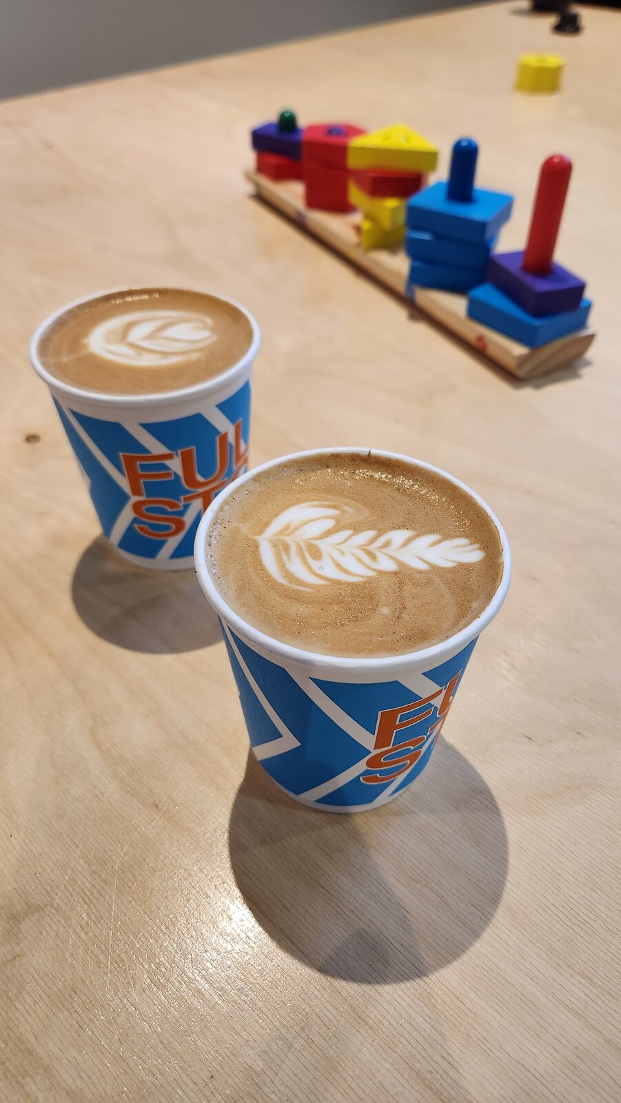 Two Full Stop coffees with latte art on a wooden café table.