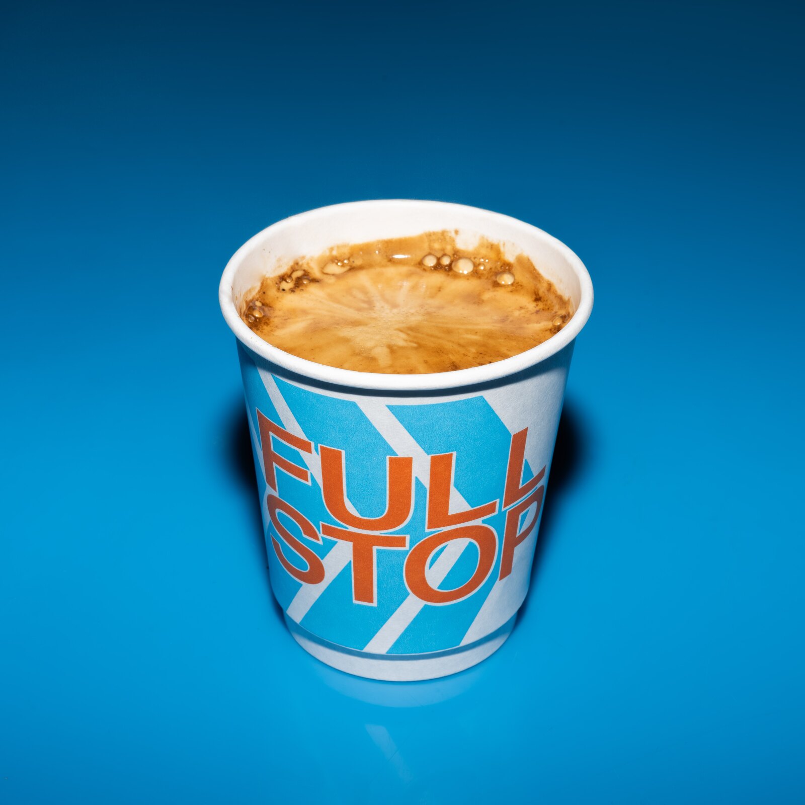 A Full Stop coffee in a branded paper cup on a bright blue background.